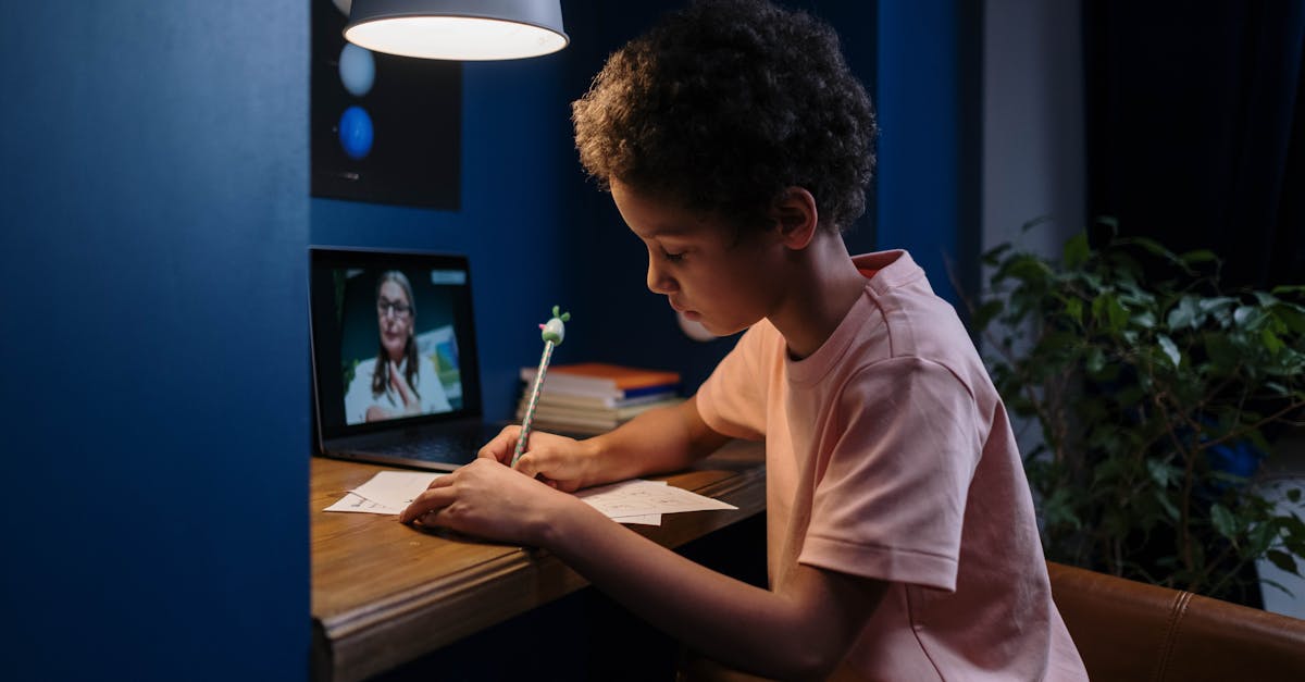 A child focused on online learning with a laptop and papers at a home desk.